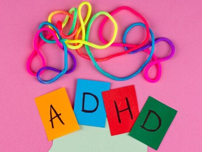 Het woord ADHD in kleurrijke viltletters onder een wirwar van gekleurde veters